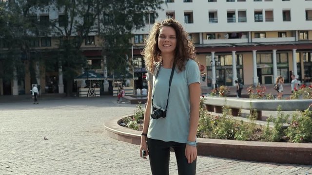 Young smiling girl with photo camera walking in city in summer