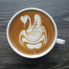 Top view of a mug of latte art coffee on timber background.