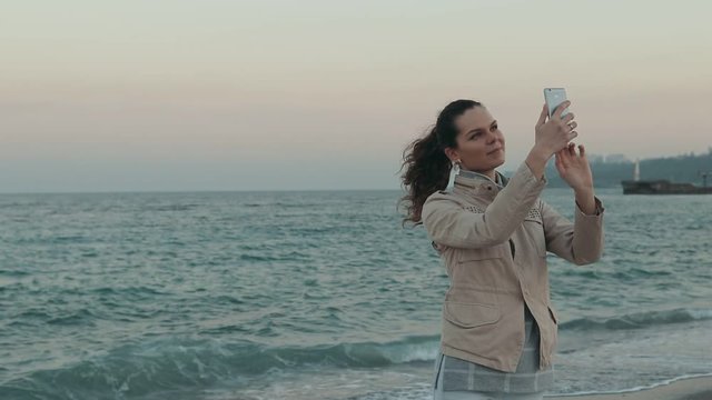 Young smiling woman taking pictures of herself in the evening on the beach