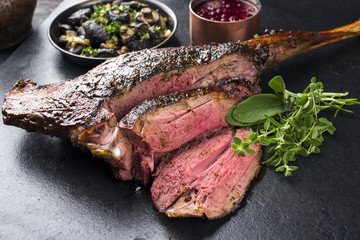 Barbecue haunch of venison with mushrooms and cranberry sauce as close-up on a slate slab - obrazy, fototapety, plakaty