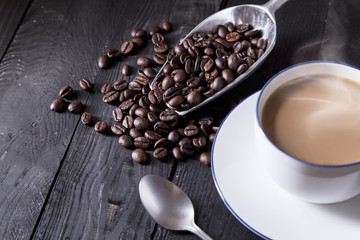 Coffee beans , hot coffee , coffee cup and metal spoon on black wood table