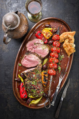 Barbecue lamb roast with skewered tomatoes and olives as close-up on a plate