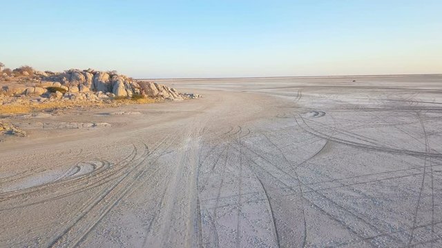 Low flight over the edge of island on large salt pan covered by tracks