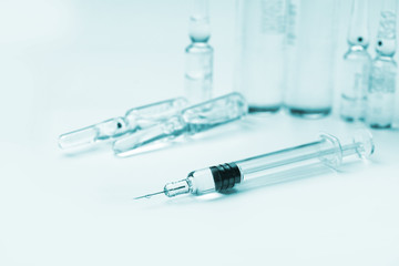 glass syringe in front of medicine bottles in blue tone