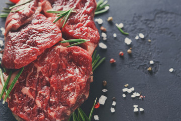 Rib eye steak and spices on wood at black background