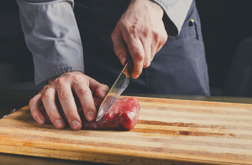 Chef cutting filet mignon on wooden board at restaurant kitchen