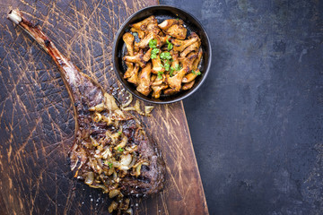 Barbecue dry aged wagyu tomahawk steak with roast onion and chanterelle as top view on old wooden board