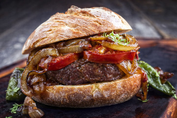 Barbecue wagyu hamburger with onions and tomatoes as close-up on a burnt cutting board