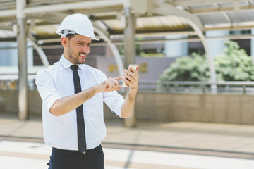 Engineer wearing safety helmet and touching smartphone with smile at construction site. concept of communication and negotiation.