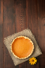 pumpkin homemade pie at wooden background decorated with burlap desk cloth top view