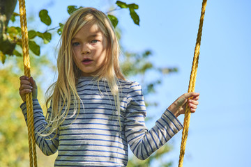 Little child blond girl having fun on a swing outdoor. Summer playground. Girl swinging high. Young child on swing in garden