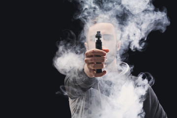 Young man vaping e-cigarette with smoke on black