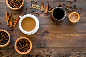 Cup of milky coffee near coffee beans and cinnamon on wooden background top view copyspace