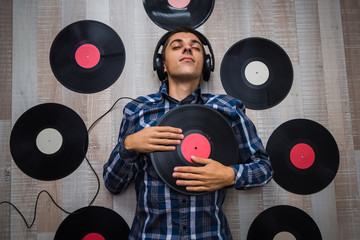 top view man (music lover) with headphones lie on the floor and listen music among retro vinyl...