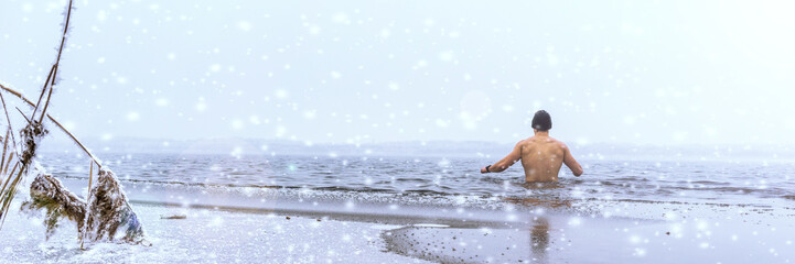 Fototapeta premium Mann beim Eisbaden im Winter, Panorama mit Schneefall