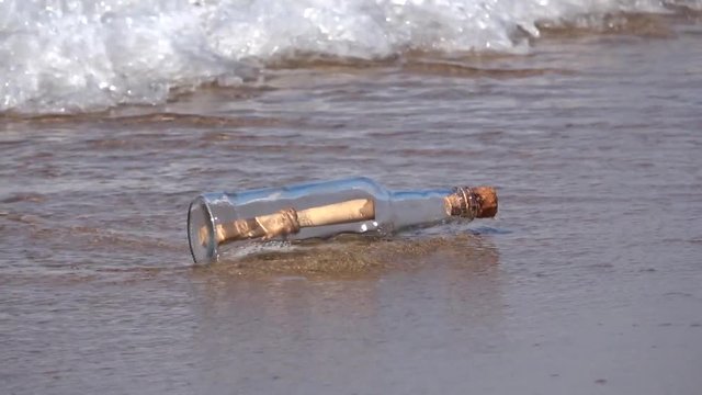 Message in bottle rolling on the sand, vacation on beach