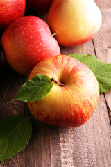 Ripe red apples with leaves on wooden background