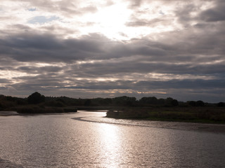 sun setting through dramatic clouds and onto lake river stream water