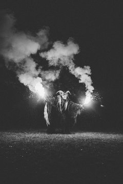 krampus with burning bengal light on a meadow