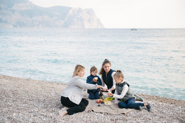 beautiful family of three generations sitting on the ground near sea on holiday picnic