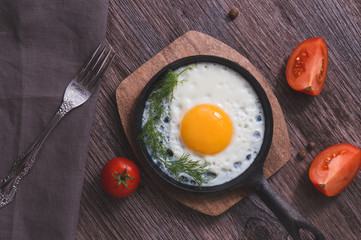 Breakfast of fried eggs in a frying pan with tomatoes and dill. Fried eggs on a wooden table top view.