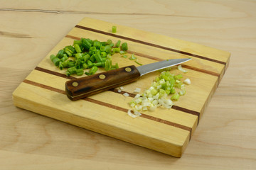 Chopped green onion scallions with green and white parts kept separate on cutting board with knife
