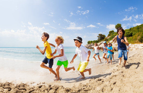 Large group of kids run on a beach along the sea