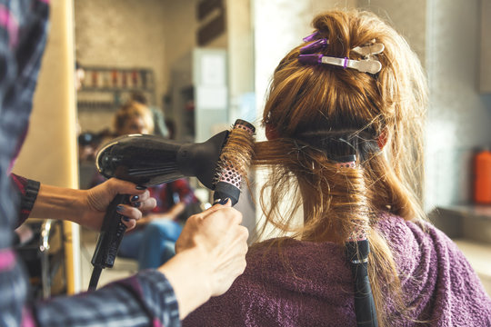 Working day inside the hair salon, hairdresser drying young woman hair with a dryer.