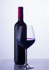 High glass with still red wine and wine bottle