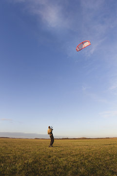 Young man kiteboarding in the field at sunset