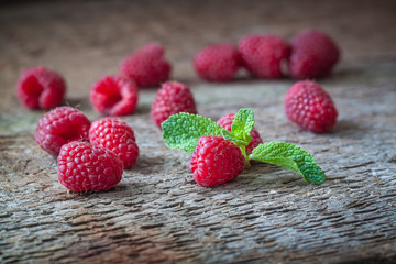Raspberries with a mint leaf on the wooden background