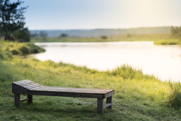 Fototapeta premium Vintage wooden Sun bed on a grass at the sunny river bank