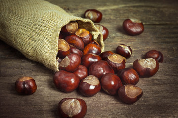 Chestnuts in jute sack on wooden background