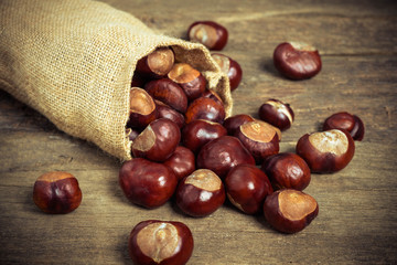 Chestnuts in jute sack on wooden background