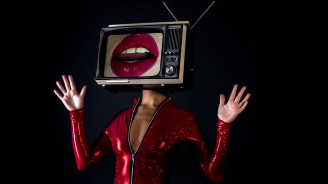 amazing woman dancing and posing with a television as a head. the tv has video of moving luscious lips on it