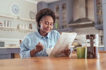 Young woman reading the newspaper while eating breakfast at home
