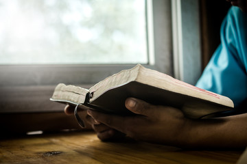 Hands of man praying and reading Bible at home