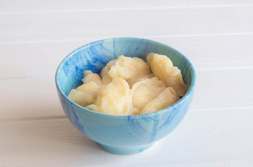 In blue ceramic dish, fruit and berry dumplings with cherries. Fresh cherry dumplings for bank. Sour cream for dumplings with cherries. Gray wooden background.