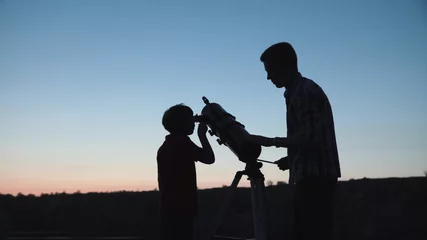 Fototapeten Anonymous man with little boy looking through telescope in twilight. © Framestock