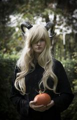 Young beautiful girl in a witch costume with horns holds a pumpkin. Halloween Theme