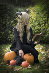 Girl in witch costume with horns enchants pumpkin. Halloween Theme