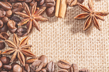 Design frame with coffee beans, cinnamon stocks on sackcloth with spices anise. Closeup image