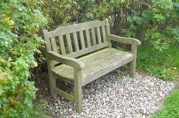 two seater park bench set on gravel with hedgerow behind