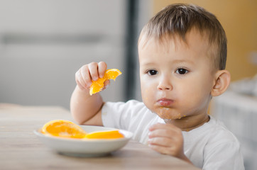 The child in the kitchen eating an orange