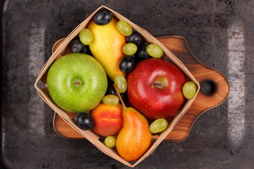 Red apple, dark blue grapes, green apple, yellow pear, green grapes, orange peach in a wooden box on a metallic background in retro style