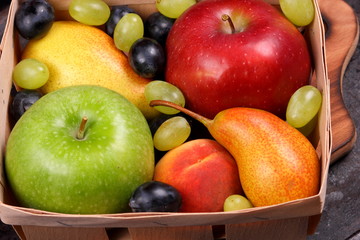 Red apple, dark blue grapes, green apple, yellow pear, green grapes, orange peach in a wooden box on a metallic background in retro style