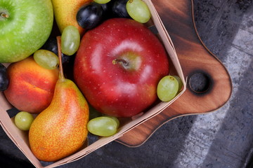 Red apple, dark blue grapes, green apple, yellow pear, green grapes, orange peach in a wooden box on a metallic background in retro style