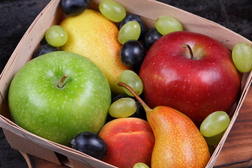 Red apple, dark blue grapes, green apple, yellow pear, green grapes, orange peach in a wooden box on a metallic background in retro style