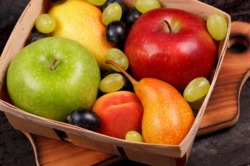 Red apple, dark blue grapes, green apple, yellow pear, green grapes, orange peach in a wooden box on a metallic background in retro style