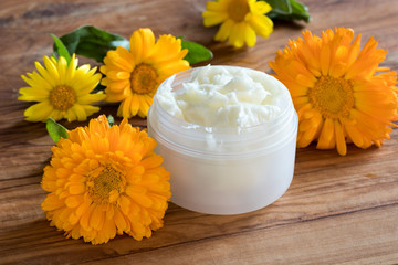 Obraz na płótnie Canvas A jar of calendula cream, with calendula flowers in the background